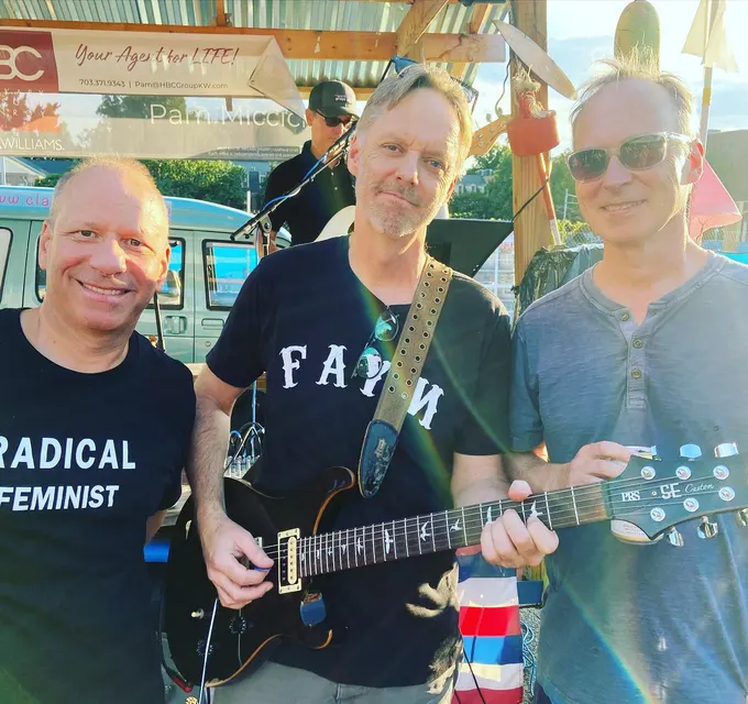 Three of the band with guitars, grinning on the Clare and Don's stage